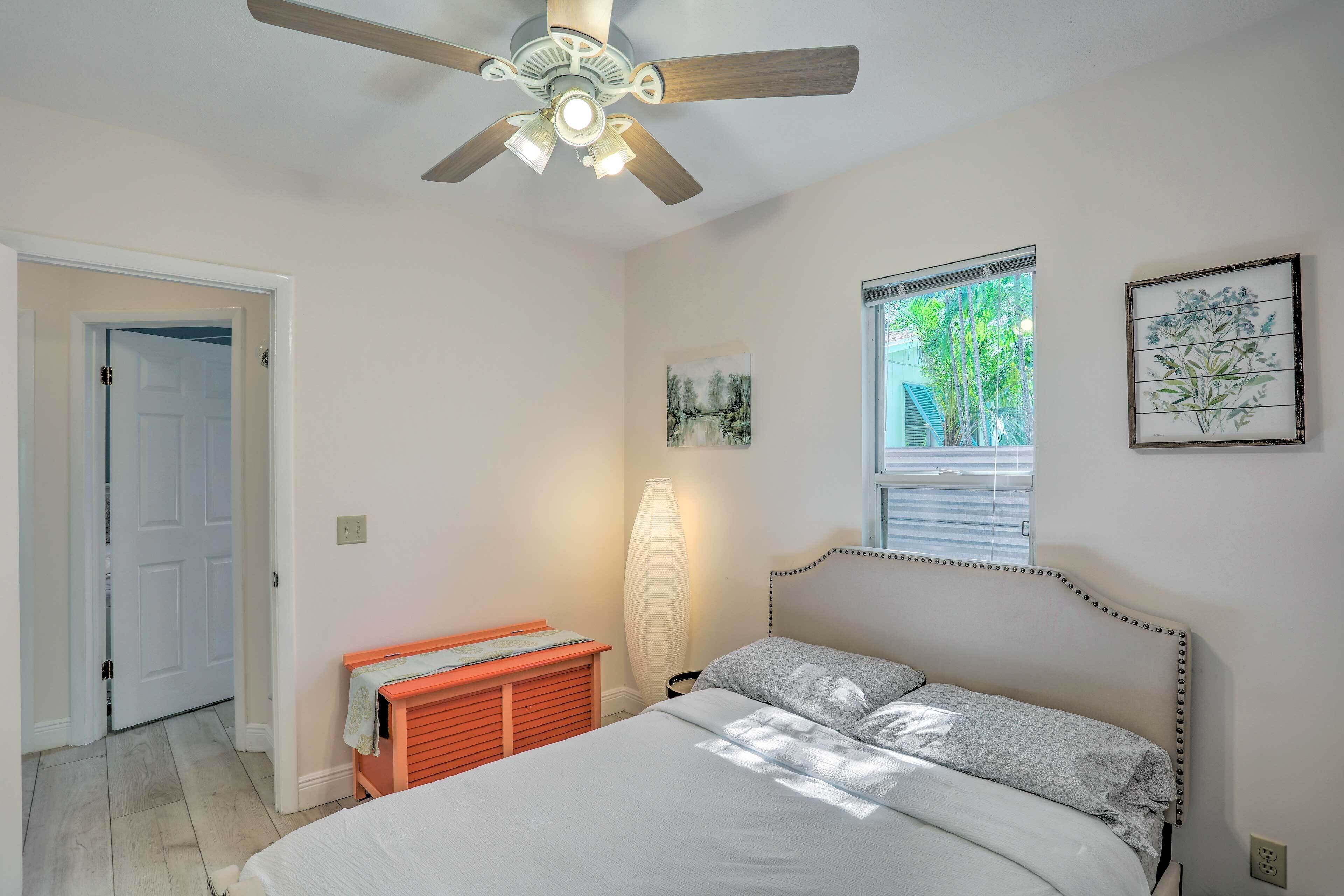 A bedroom with a bed, a ceiling fan, a window with a view, and a door.