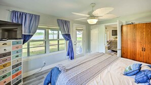Quarto com cama, ventilador de teto, cômoda com gavetas e vista para o exterior através de uma janela.