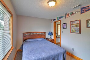 Quarto com cama, mesa de cabeceira, luminária, espelho e janela com persianas.