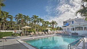 Une piscine entourée de chaises longues et de parasols, bordée de palmiers et d’un bâtiment doté d’un toit bleu.