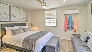 Een slaapkamer met een bed, een bankje, een slaapbank en een plafondventilator, plus een airconditioning.