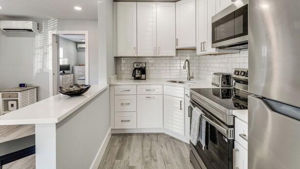 A modern kitchen with white cabinets, stainless steel appliances, and a wooden floor. - Walk to Gulf: Madeira Beach Condo w/ Patio (Madeira Beach)