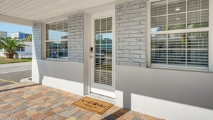 A building with a white exterior, stone accents, and a welcome mat at the entrance. - Walk to Gulf: Madeira Beach Condo w/ Patio (Madeira Beach)