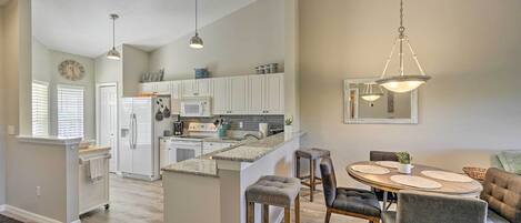 A spacious kitchen with white cabinets, a central island, and a dining area with a round table and bar stools.