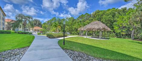 A pathway leading to a gazebo surrounded by lush greenery and a building with a red roof.