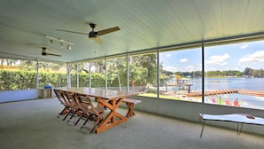 A spacious room with a large table and chairs, a ceiling fan, and large windows overlooking a body of water and dock.