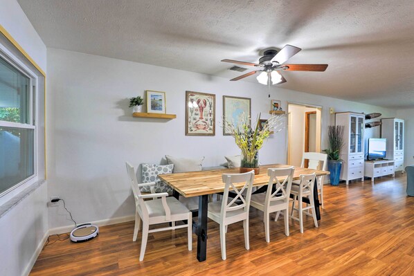 A dining area with a wooden table, white chairs, a ceiling fan, and a small robot vacuum cleaner.