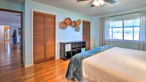 A bedroom with a bed, wooden floor, a ceiling fan, and a window with curtains.
