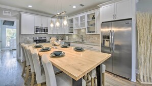 Une cuisine moderne avec des meubles blancs, des appareils en acier inoxydable et une table à manger en bois.