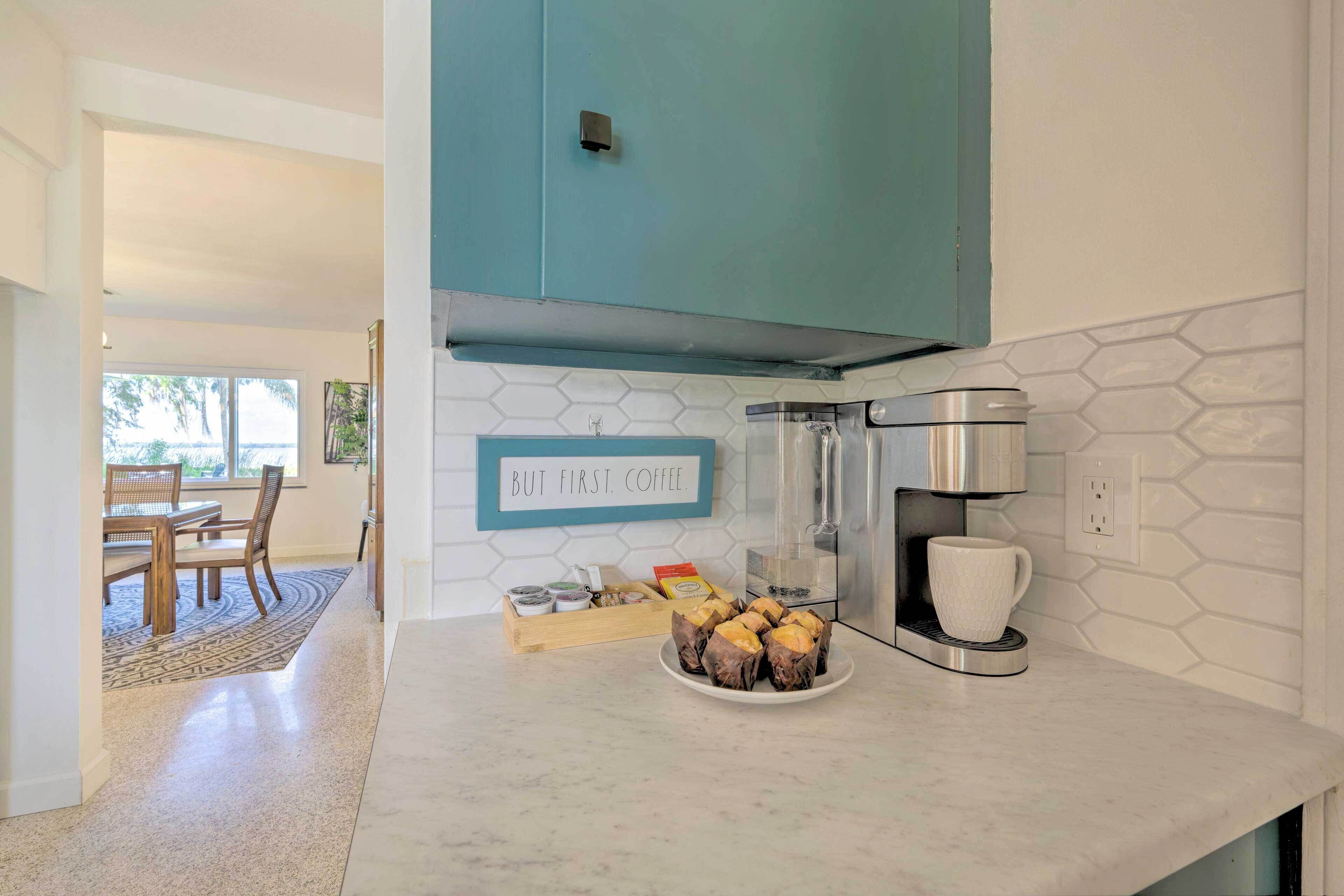 A kitchen with a coffee maker, a plate of muffins, and a sign that says "But first, coffee."