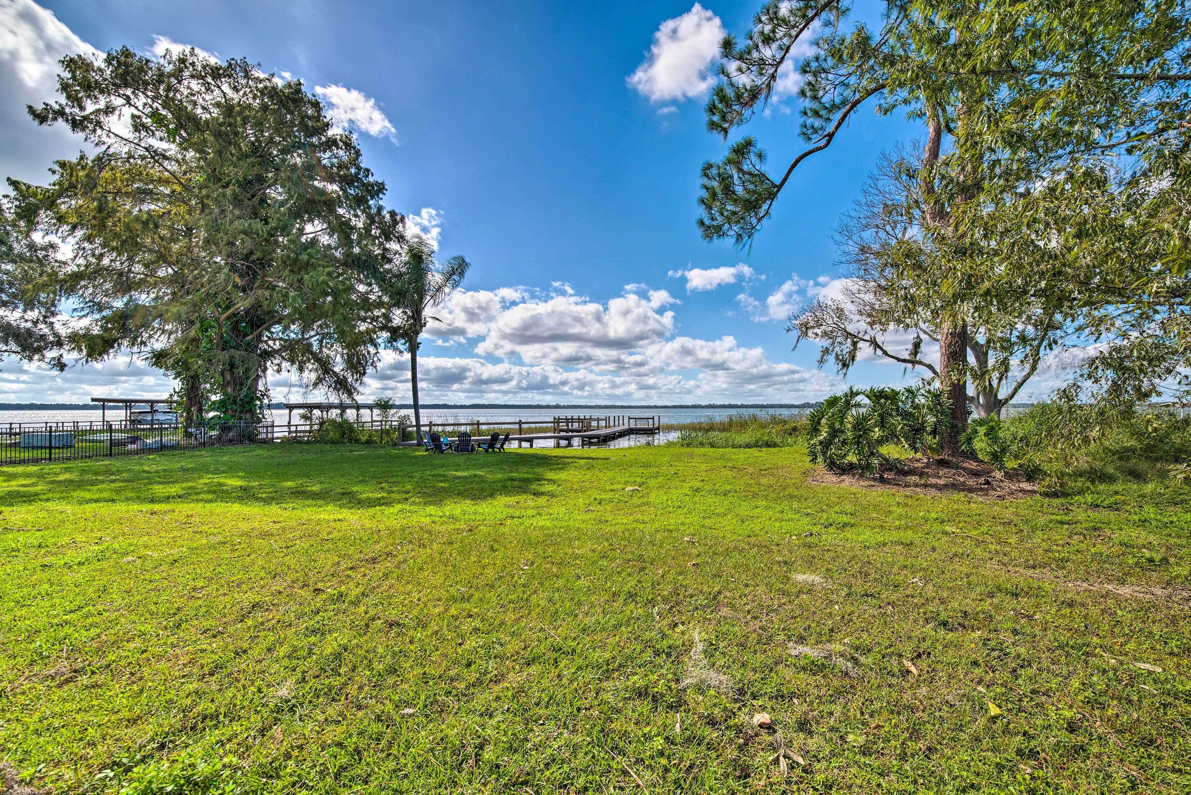 A grassy park with trees, a wooden dock, and a view of the water.