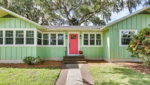 A green house with a red door, white windows, and a brick pathway leading to the entrance. - Walk to Lakes! Tropical Escape in Mount Dora (Mount Dora)