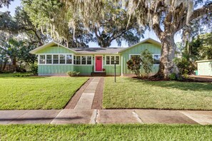 A green house with a red door, surrounded by a well-maintained lawn and large trees. - Walk to Lakes! Tropical Escape in Mount Dora (Mount Dora)