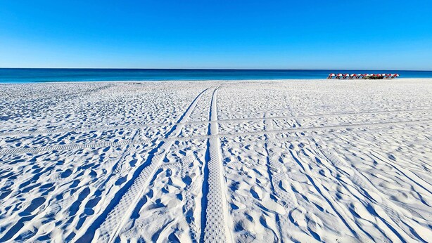 Una playa con cielo despejado y una hilera de sombrillas a lo lejos.