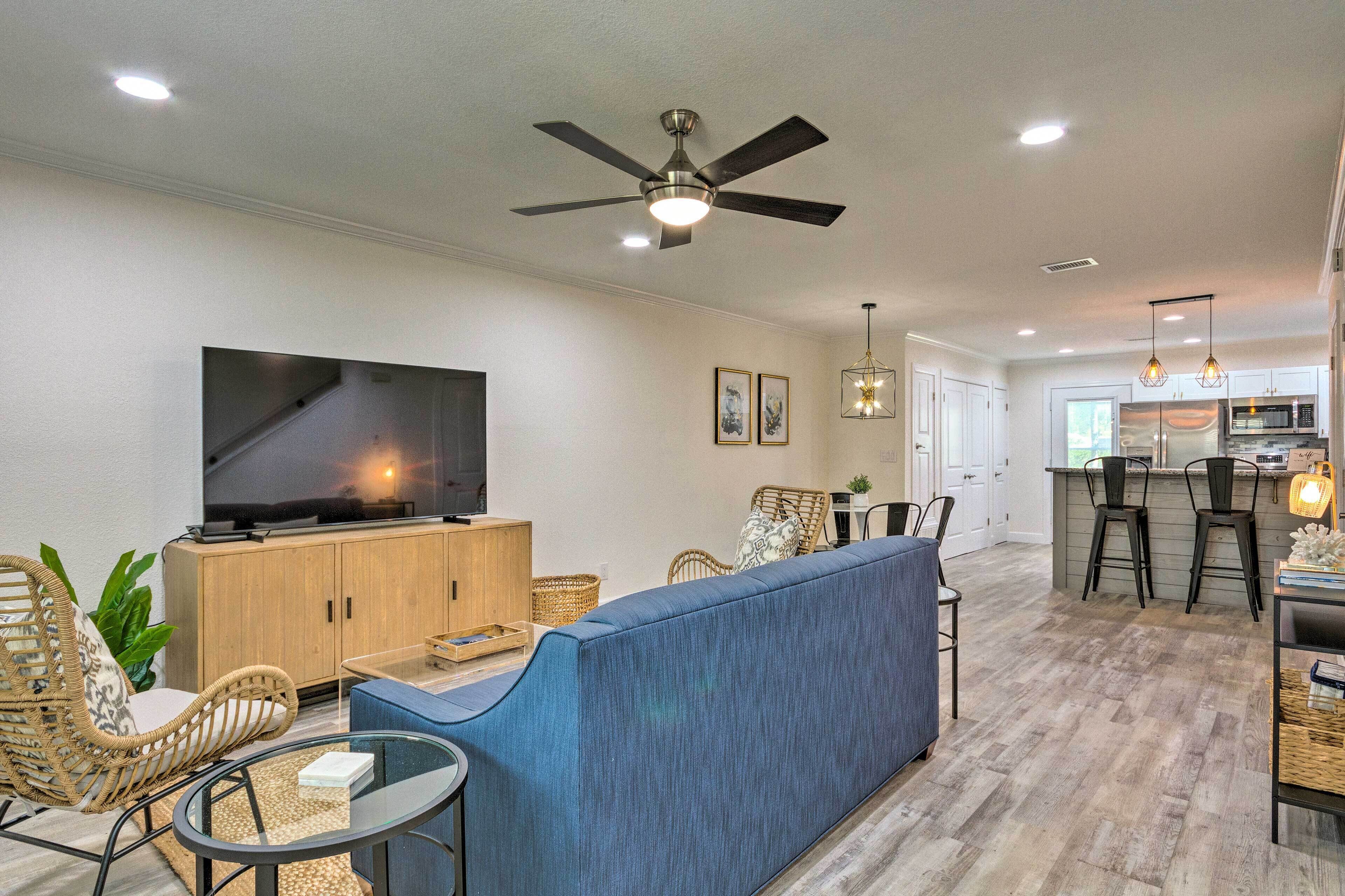 A modern living room with a TV, sofa, and chairs. There is a kitchen area with a bar and stools.