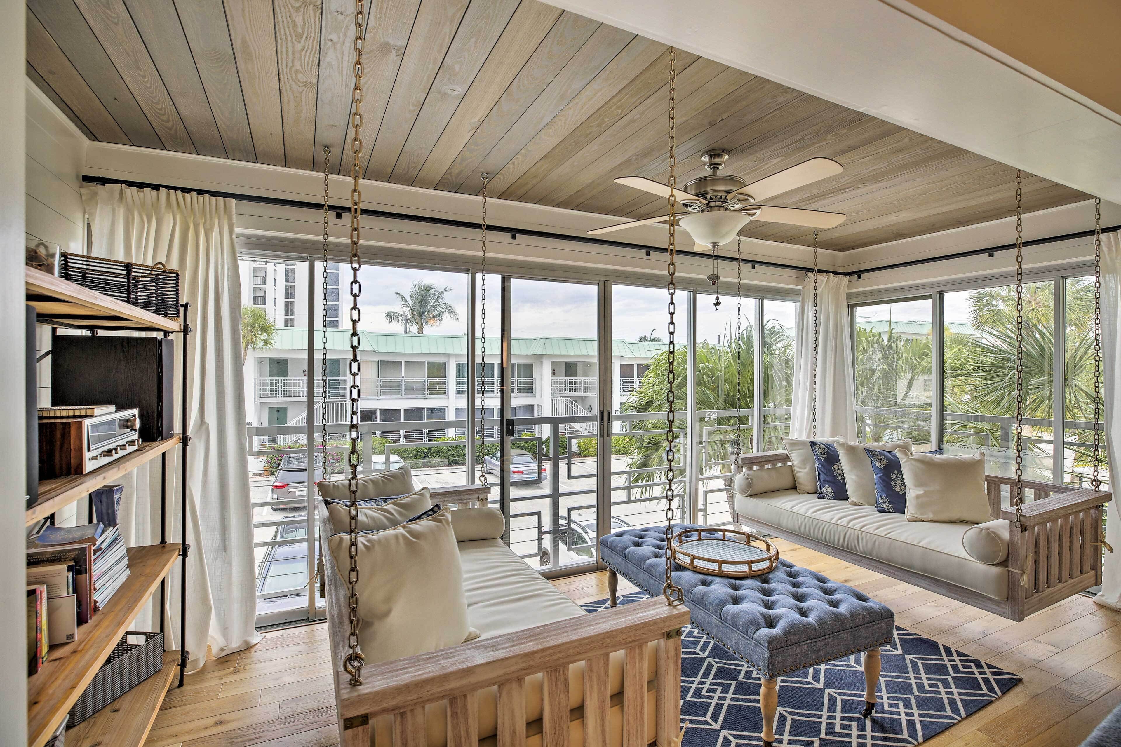 A spacious living area with a wooden ceiling, large windows, a swing chair, and a sofa with cushions.