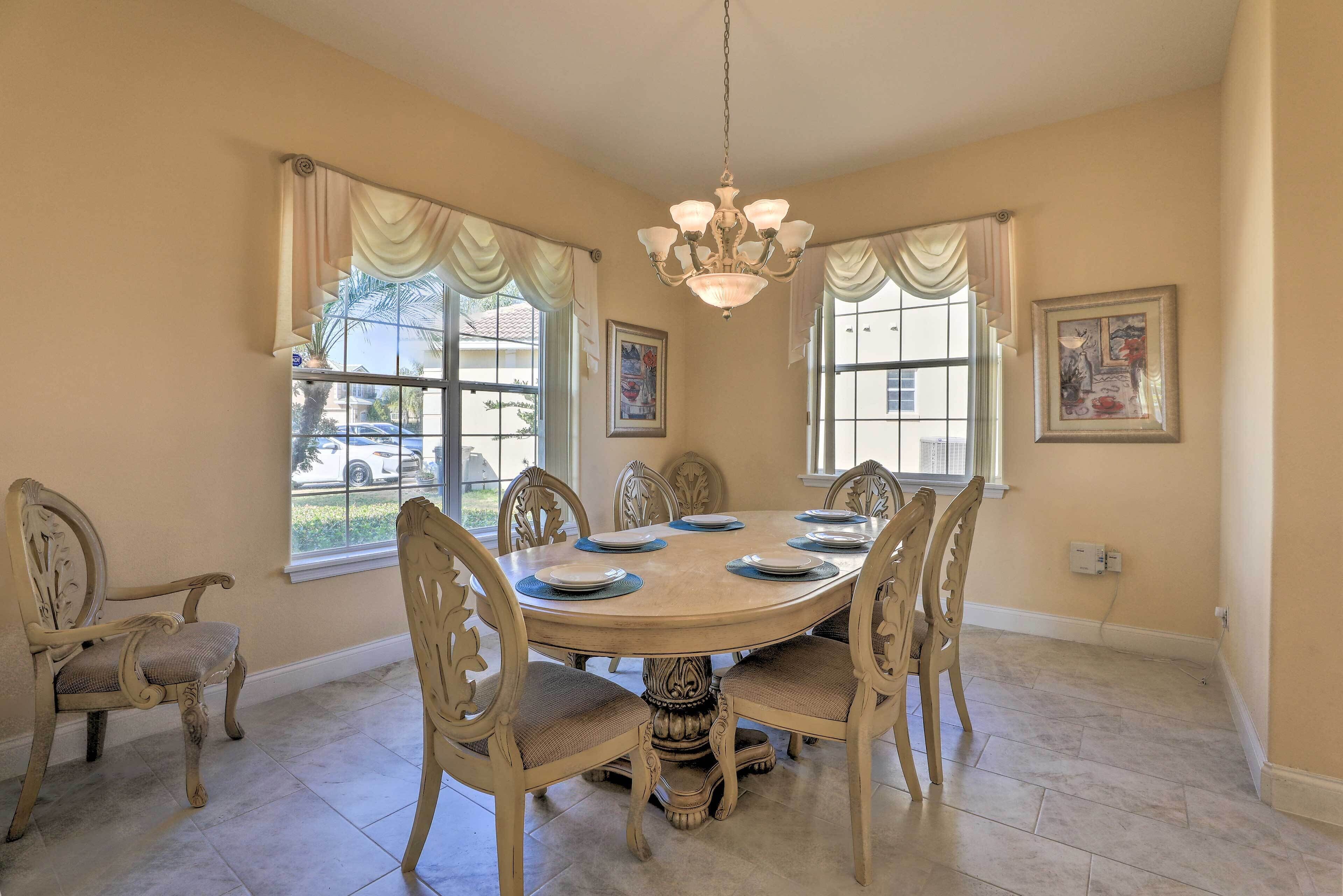 A dining room with a round table, six chairs, and a chandelier.