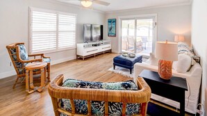 A living room with a ceiling fan, a television, wicker furniture, and a white sofa.