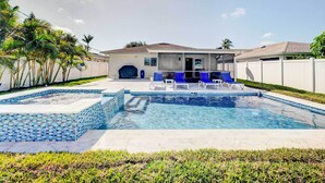 A swimming pool with a tiled deck, a covered hot tub, and a patio area with lounge chairs.