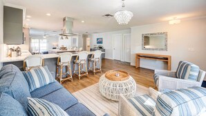 A spacious living area with a sofa, chairs, a round coffee table, and a dining area with a kitchen in the background.