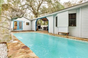 Un área de piscina con borde de piedra, un porche cubierto y una casa con detalles azules.