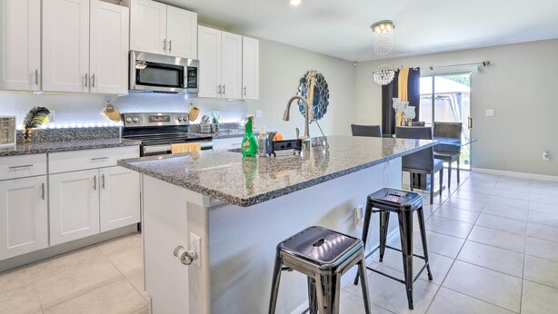 A modern kitchen with white cabinets, a stainless steel microwave, a granite countertop, and a bar area with stools.