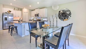 A modern kitchen with white cabinets, a stainless steel refrigerator, and a glass dining table with black chairs.