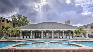 A hotel with a swimming pool, lounge chairs, and a covered area with a roof.