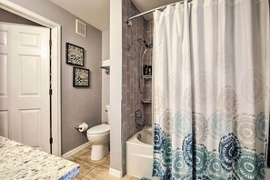 Ein Badezimmer mit Toilette, einer Badewanne und einer Dusche. An der Wand befinden sich Bilder in Rahmen und eine weiße Tür.