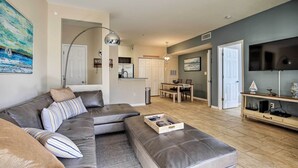 A modern living room with a grey sectional sofa, a wooden coffee table, and a flat-screen TV mounted on the wall.