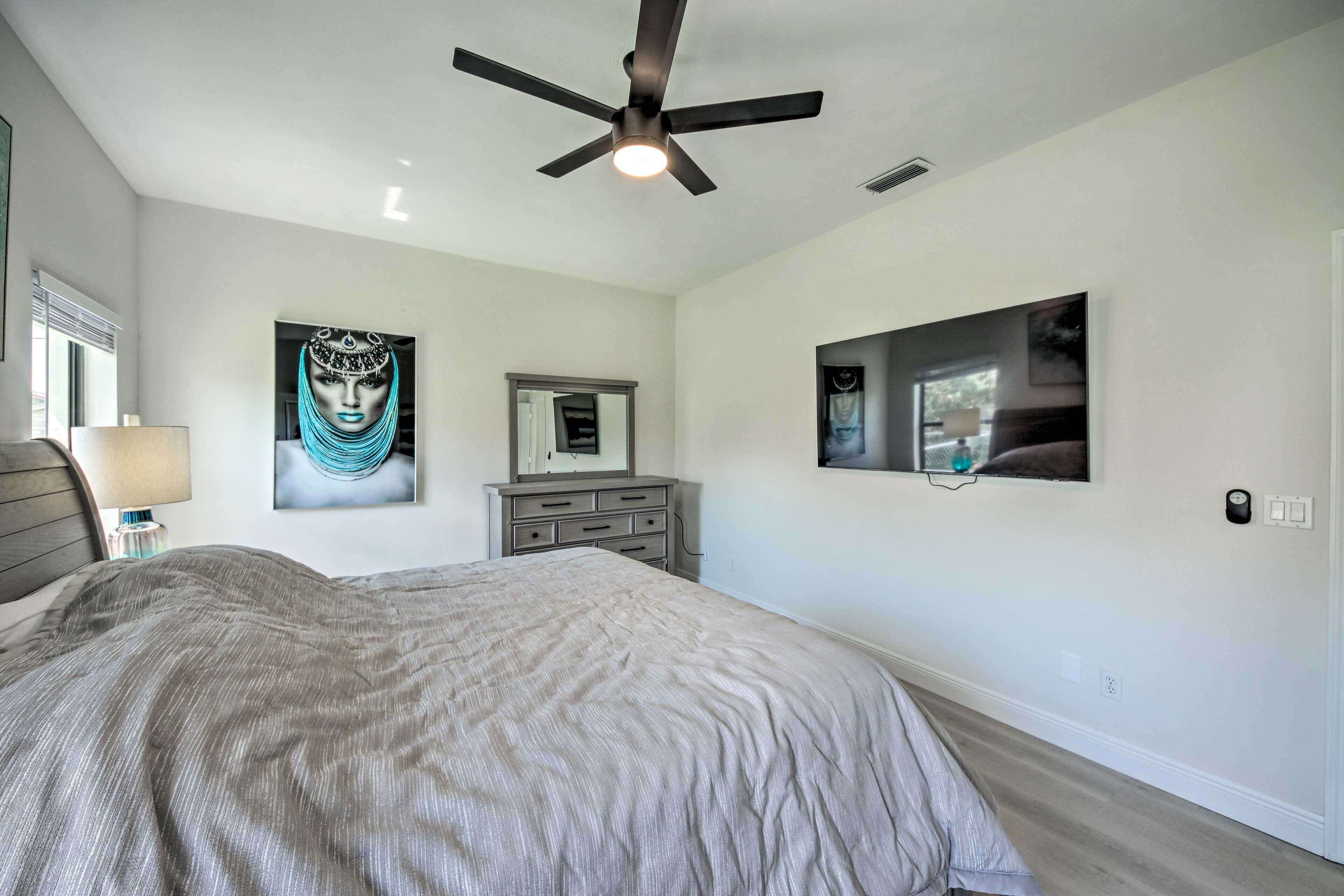 A bedroom with a bed, a ceiling fan, a dresser, and wall art.