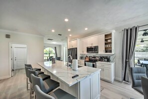 A modern kitchen with white cabinets, a marble island, and bar stools. - Lanai + Pool: Dog-friendly Home in Cape Coral! (Cape Coral)