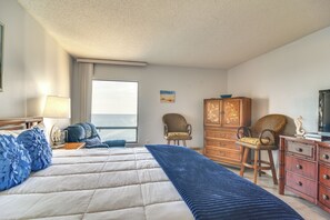 A bedroom with a large bed, a dresser, a chair, and a window with a view of the sea. - Dolphin & Manatee Viewing From 15th Floor (Clearwater Beach)