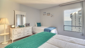 A bedroom with a bed, a dresser, a mirror, and a window with a view of buildings and the sea. - Dolphin & Manatee Viewing From 15th Floor & Pool! (Clearwater Beach)