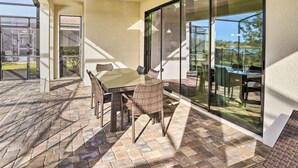 A patio area with a glass door leading to a garden, a table with chairs, and a brick floor. - Modern Haines City Home w/ Pool & Lanai! (Haines City)