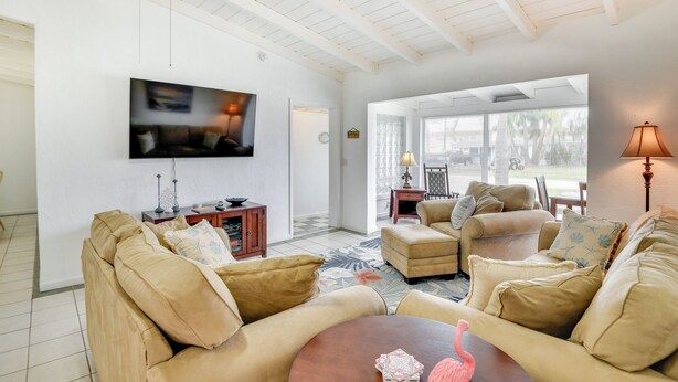 A spacious living room with a high ceiling, a flat-screen TV mounted on the wall, and a cozy seating area with sofas and a coffee table. - Ormond Beach Vacation Rental - Walk to Ocean! (Ormond Beach)