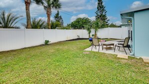 A backyard with a white fence, a patio with chairs and a table, and a house with a blue exterior. - Ormond Beach Vacation Rental - Walk to Ocean! (Ormond Beach)