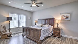 A bedroom with a wooden bed, a ceiling fan, a window with blinds, a nightstand with a lamp, and a chair. - Palm Bay Home w/ Patio & Yard - 12 Mi to Beach! (Palm Bay)