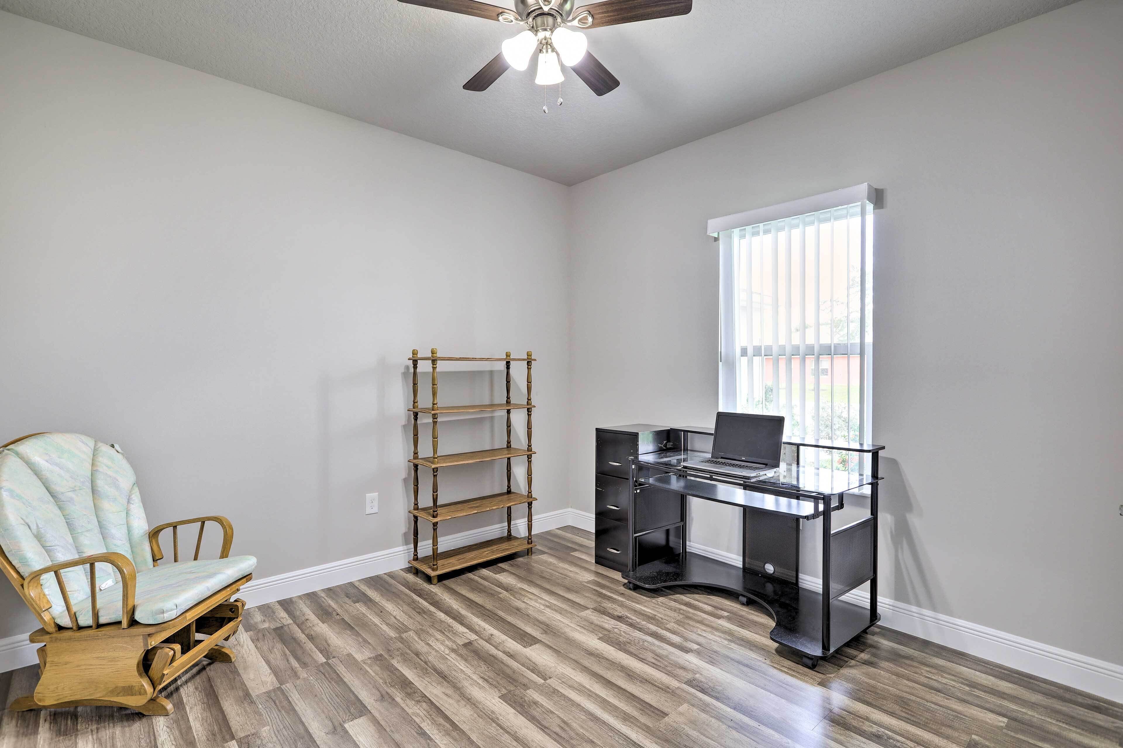 A room with a wooden floor, a desk with drawers, a chair, a bookshelf, and a window with blinds.