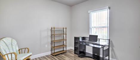 A room with a wooden floor, a desk with drawers, a chair, a bookshelf, and a window with blinds.