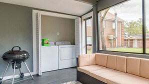 Ein Waschraum mit Waschmaschine und Trockner, ein Grill und ein beiges Sofa in der Nähe eines großen Fensters.