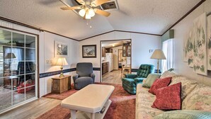 A spacious living room with a ceiling fan, a sofa, a chair, and a coffee table. There is a sliding glass door leading to a patio area. - Peaceful Canal-front Retreat w/ Boathouse! (Leesburg)