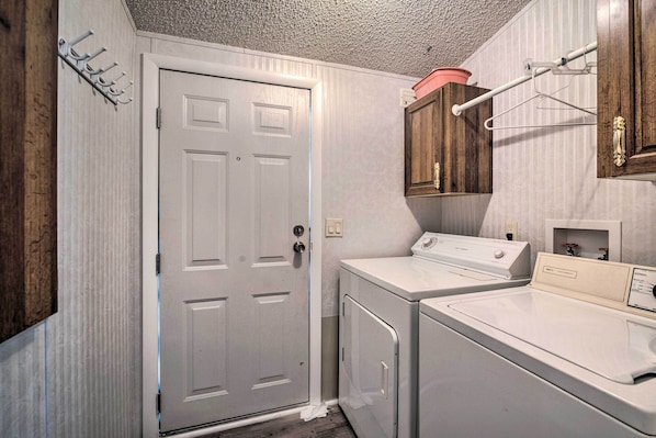 A laundry room with two washers and dryers, a wooden cabinet, and a door. - Peaceful Canal-front Retreat w/ Boathouse! (Leesburg)