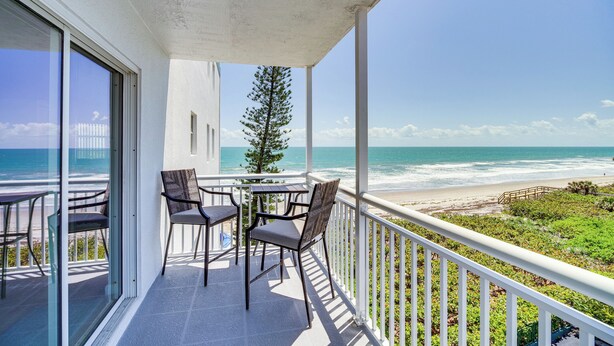 Ein Balkon mit Tisch und Stühlen mit Blick auf einen Strand.