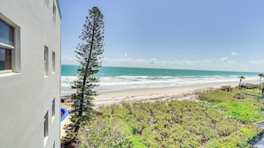 Blick auf einen Strand mit einem Gebäude, dem Meer und Pflanzen.