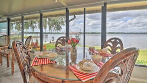 Uma sala de jantar com mesa de vidro, cadeiras e vista para um lago.