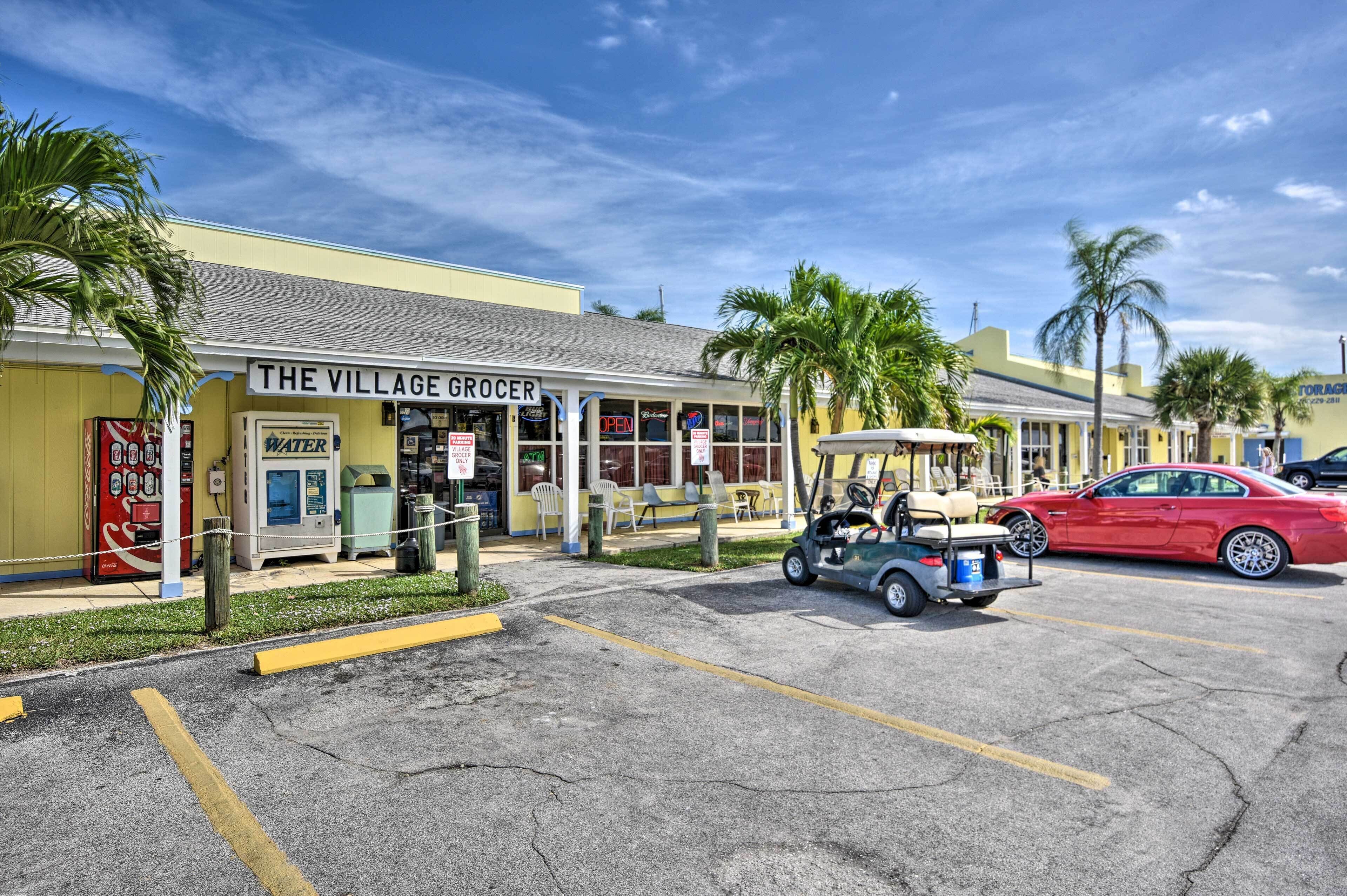 Un estacionamiento con un carrito de golf, un auto rojo y un edificio con la leyenda 'The Village Grocer'.