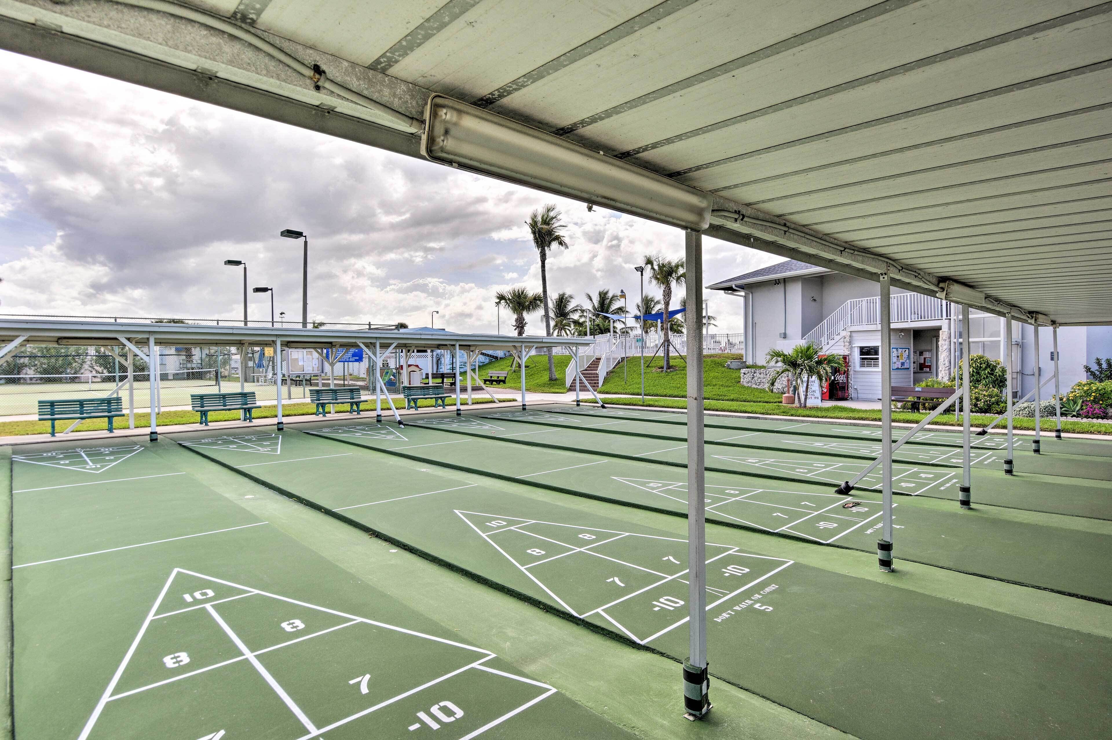Un terrain de jeu de shuffleboard en plein air, doté d’un revêtement en feutre vert, de marquages blancs et de poteaux en métal.