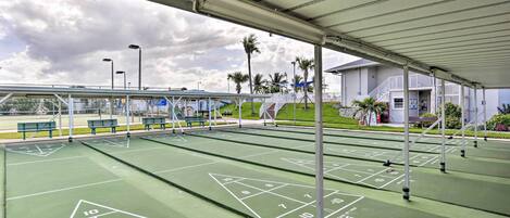 Un terrain de jeu de shuffleboard en plein air, doté d’un revêtement en feutre vert, de marquages blancs et de poteaux en métal.