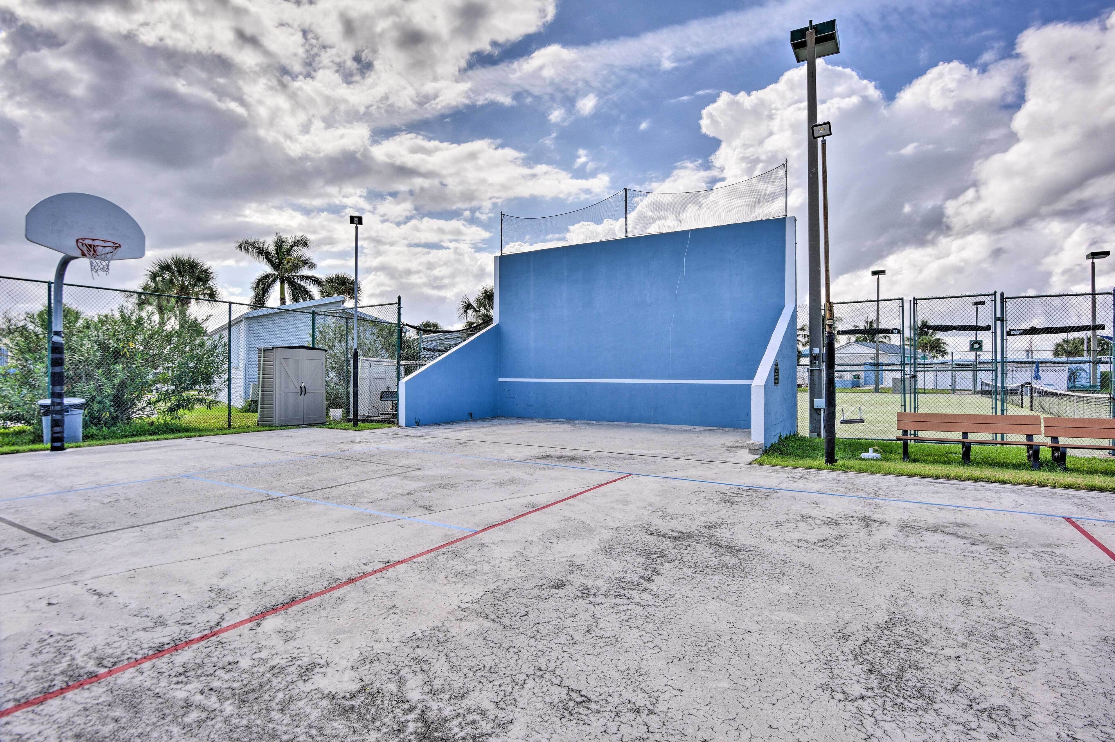 An outdoor basketball court with a blue wall, a basketball hoop, and a bench.